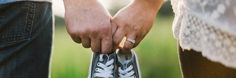 Ehepaar hält Händchen und hat Babyschuhe in der Hand